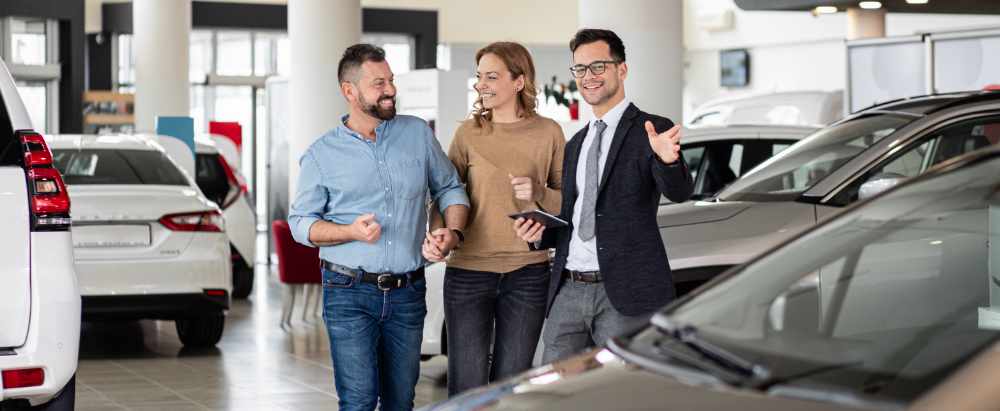 Salesman dressed smartly in a suit showing a happy couple cars within a showroom.