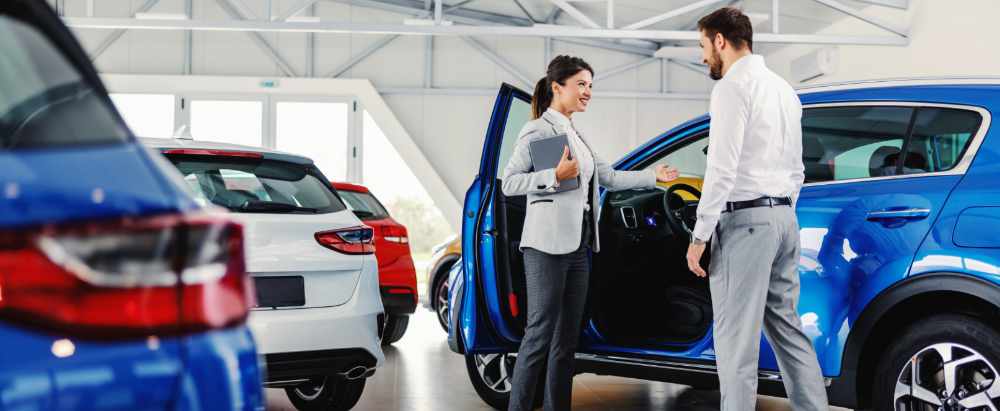 Friendly, smiling female seller showing brand new car to a customer while standing in car salon.