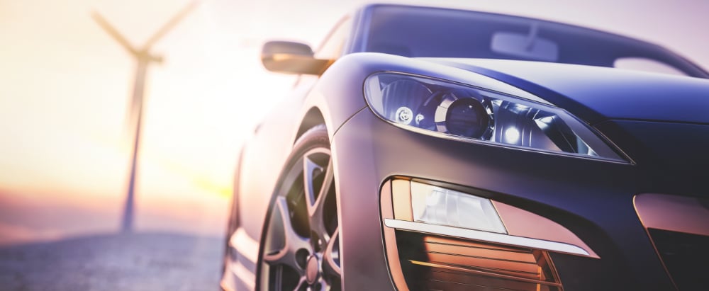 The image in front of the sports car scene behind as the sun going down with wind turbines in the back.