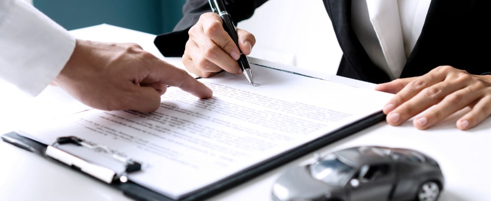 Closeup of Asian female signing car insurance document or lease paper contract or agreement. Buying or selling new or used vehicle with car keys on table.